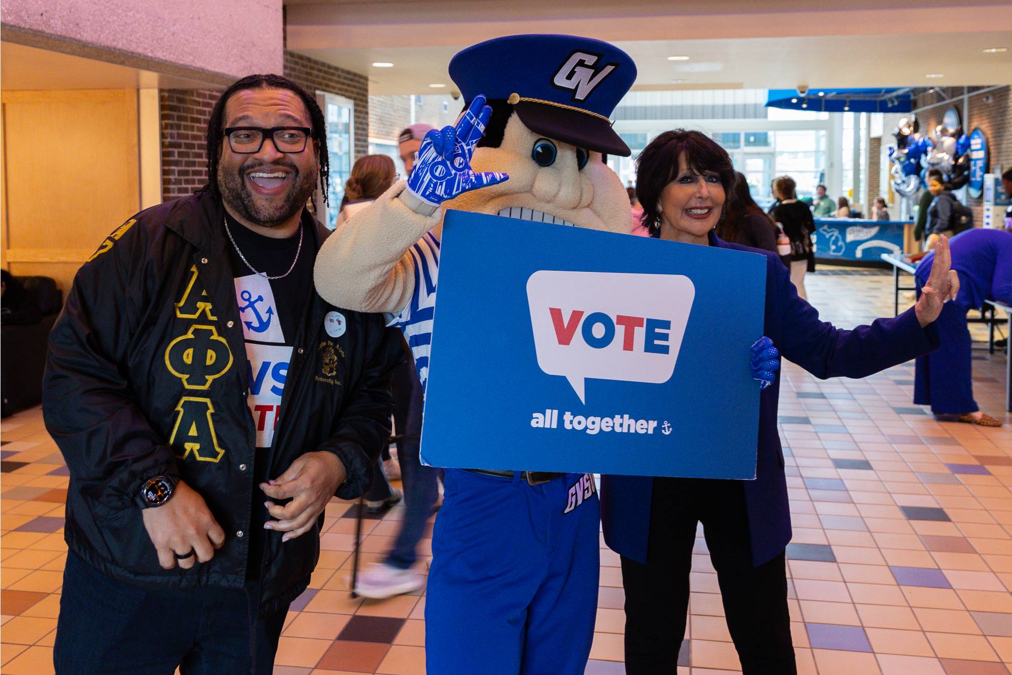 Louie the Laker holding up a foam core sign that says "Vote! all together"